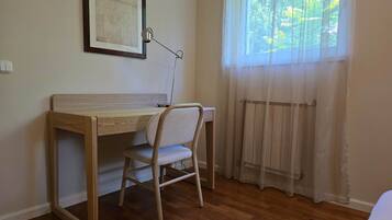 Une pièce avec un bureau en bois, une chaise, un radiateur et une fenêtre ornée de rideaux légers.