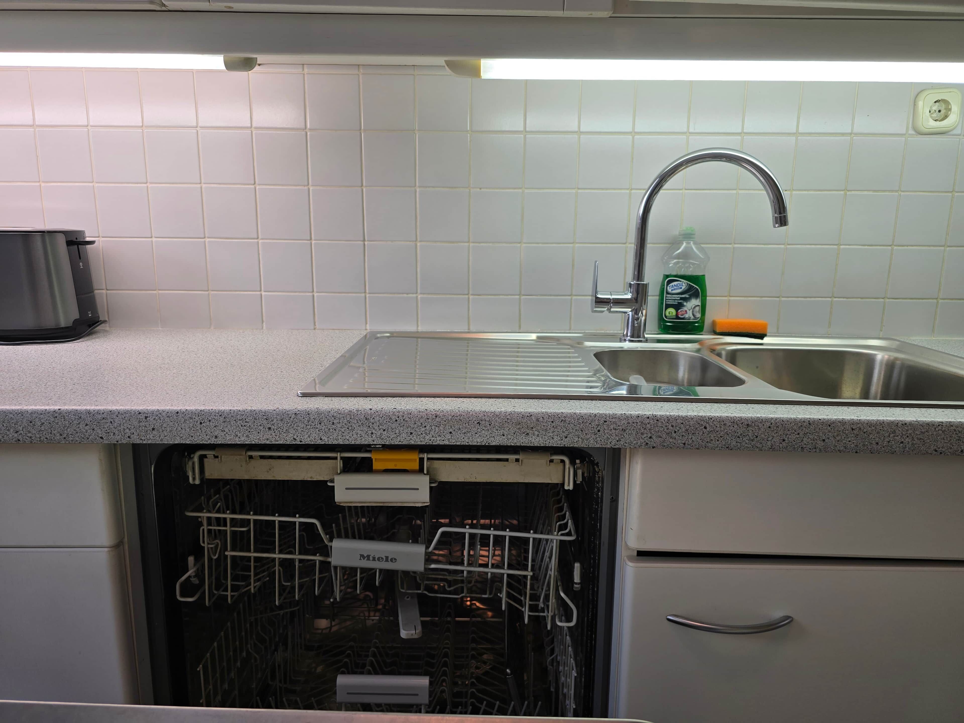 Una cucina con lavello in acciaio inossidabile, portaoggetti per piatti e una bottiglia di detersivo per piatti.