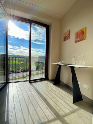 A room with a large sliding glass door, a table with glasses and a bottle, and two abstract paintings on the wall. - Le Cornici - Homes (Piemonte)