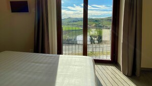 Habitación de hotel con una cama grande, vista de un paisaje a través de un cristalero corredero y un televisor pequeño en la pared.