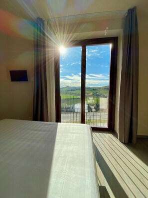 A hotel room with a bed, curtains, and a view of a landscape through a large window. - Le Cornici - Homes (Piemonte)