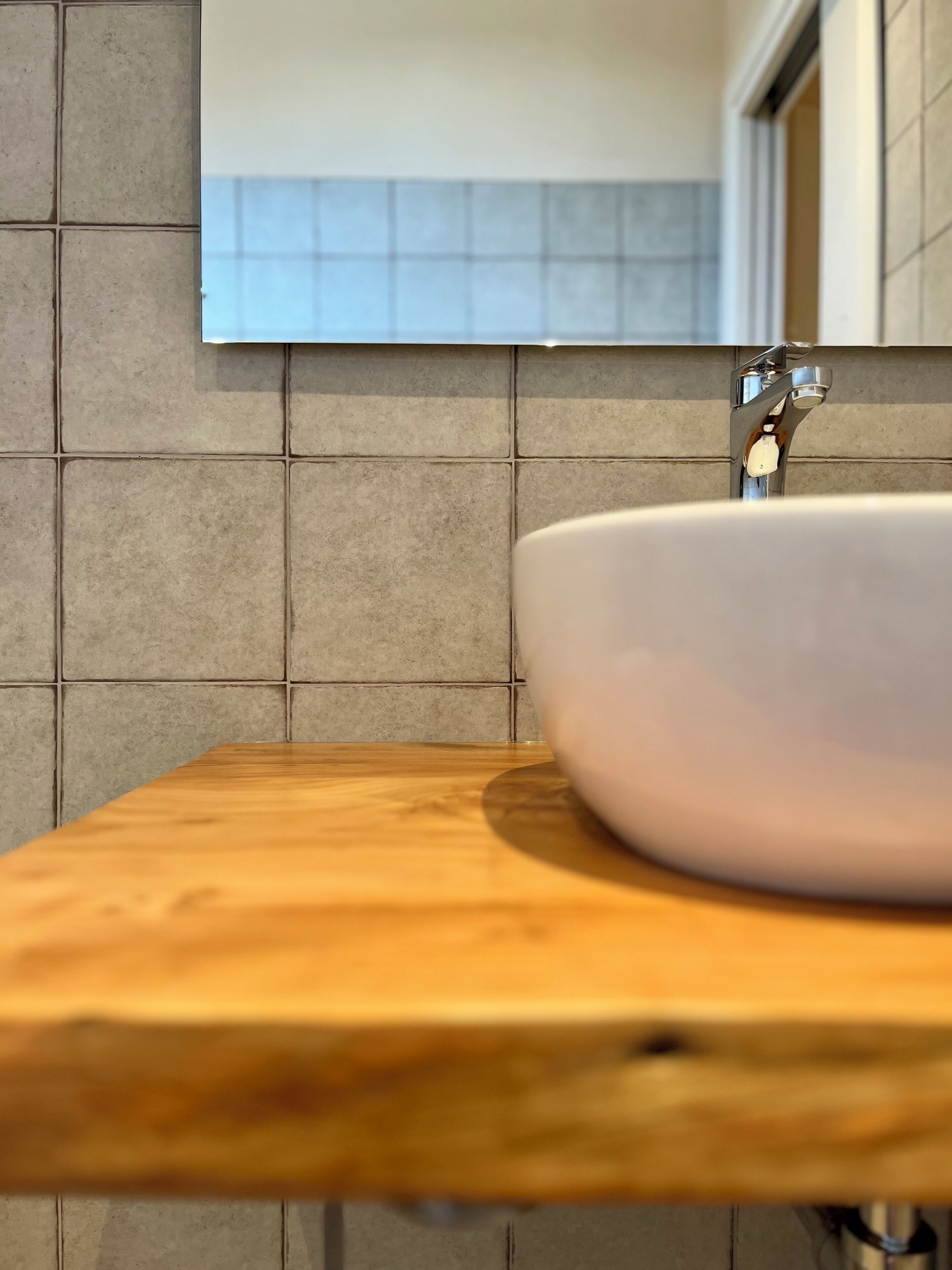 A bathroom with a wooden countertop, a white sink, and a tiled wall.