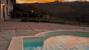 Una piscina con deck de piedra, un edificio con balcón y vista al atardecer.