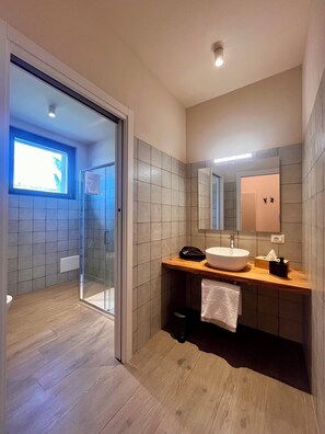 Un baño moderno con mampara de vidrio, tocador de madera, un espejo grande y vista al exterior.