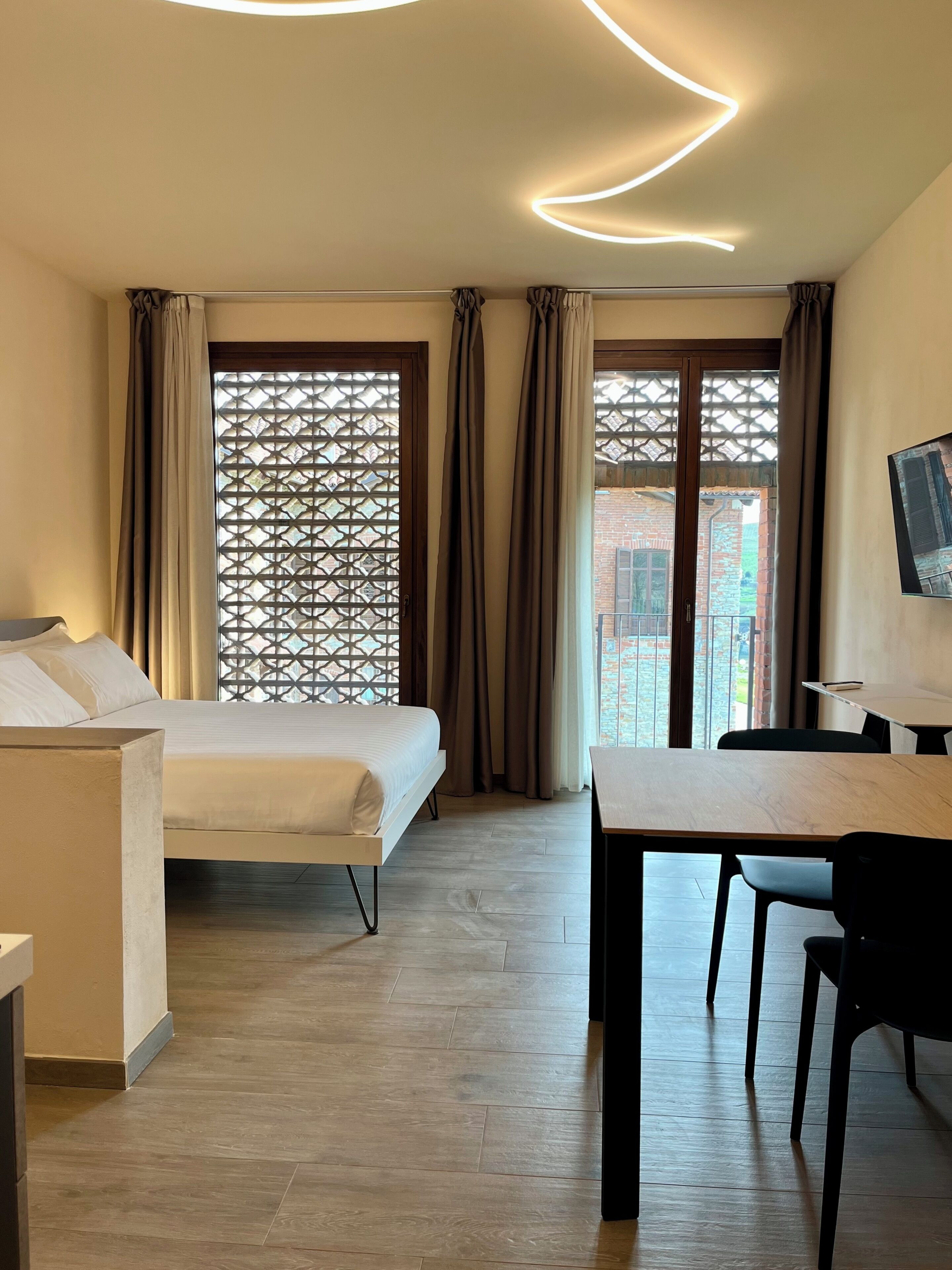 A modern hotel room with a bed, a desk, and a view of a brick building.
