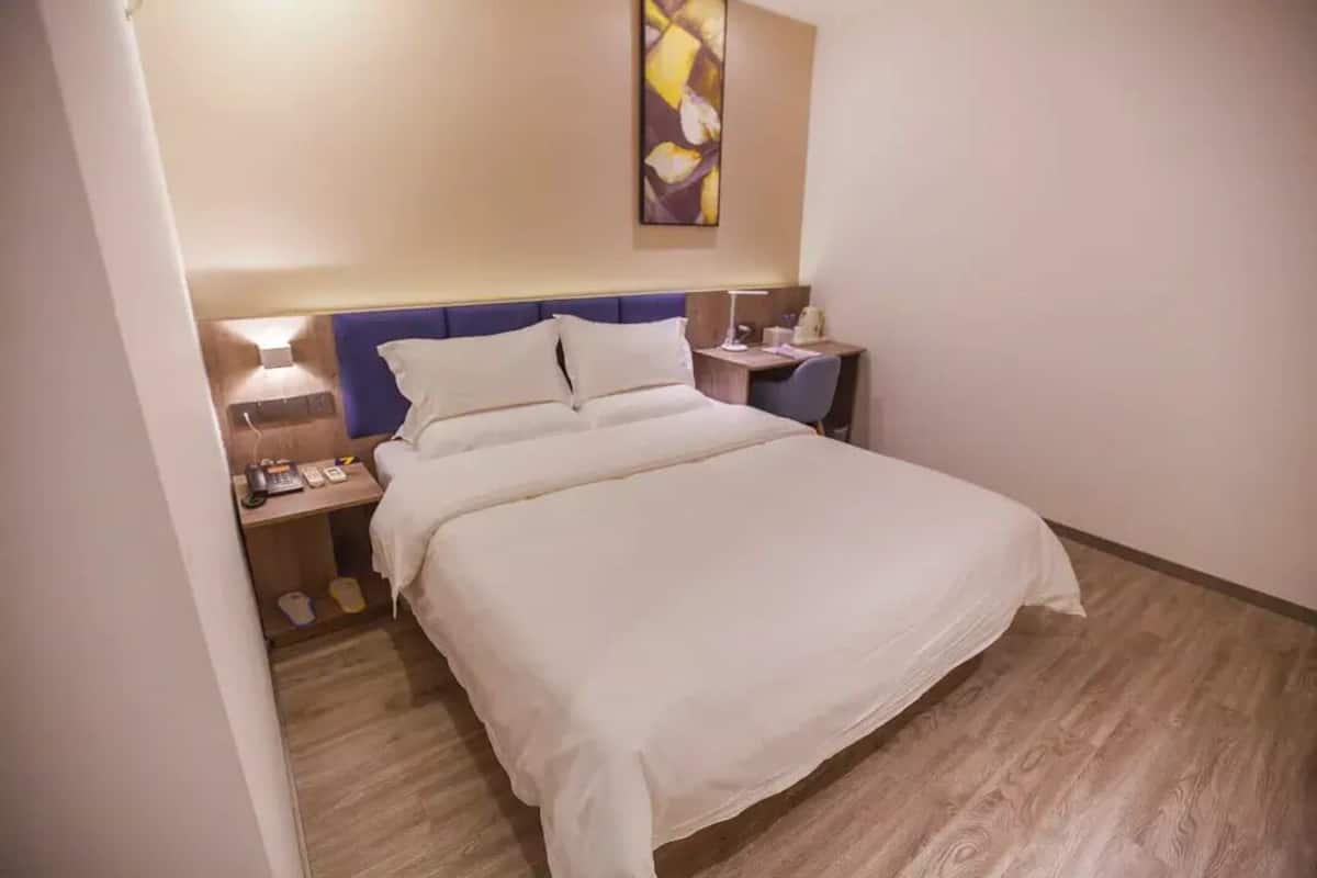 Quarto de hotel com cama, mesas de cabeceira, escrivaninha e uma obra de arte na parede.