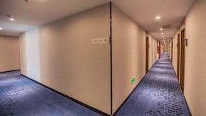 A hotel hallway with a carpeted floor, a door with a green emergency exit sign, and a long corridor with doors on one side. - QīTiānYōupǐnZhāngjiājièDàyōngGǔchéngDiàn (Zhangjiajie)