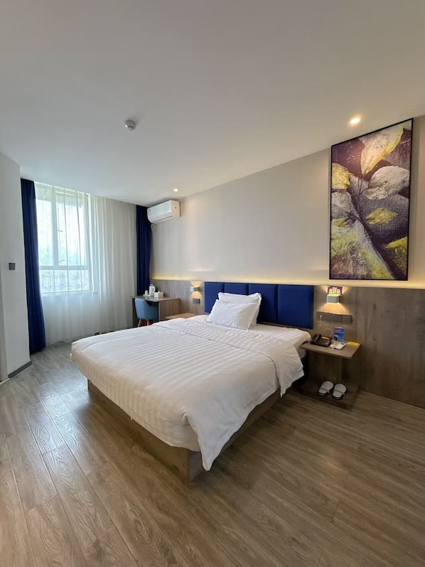 A modern hotel room with a large bed, a desk, a chair, a bedside table with a lamp, and a large window with curtains. - QīTiānYōupǐnZhāngjiājièDàyōngGǔchéngDiàn (Zhangjiajie)