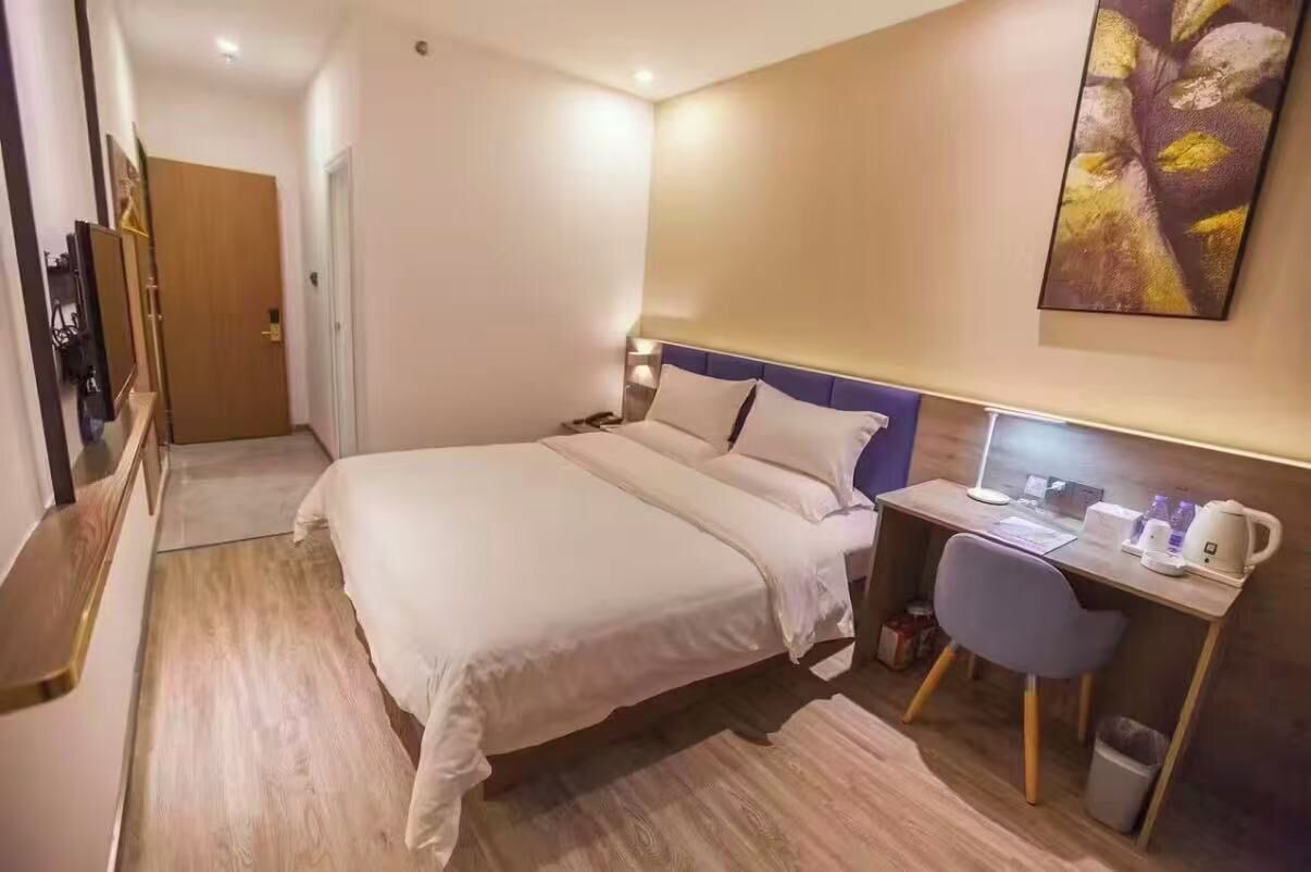 Una habitación de hotel con cama, escritorio, silla y un cuadro en la pared.