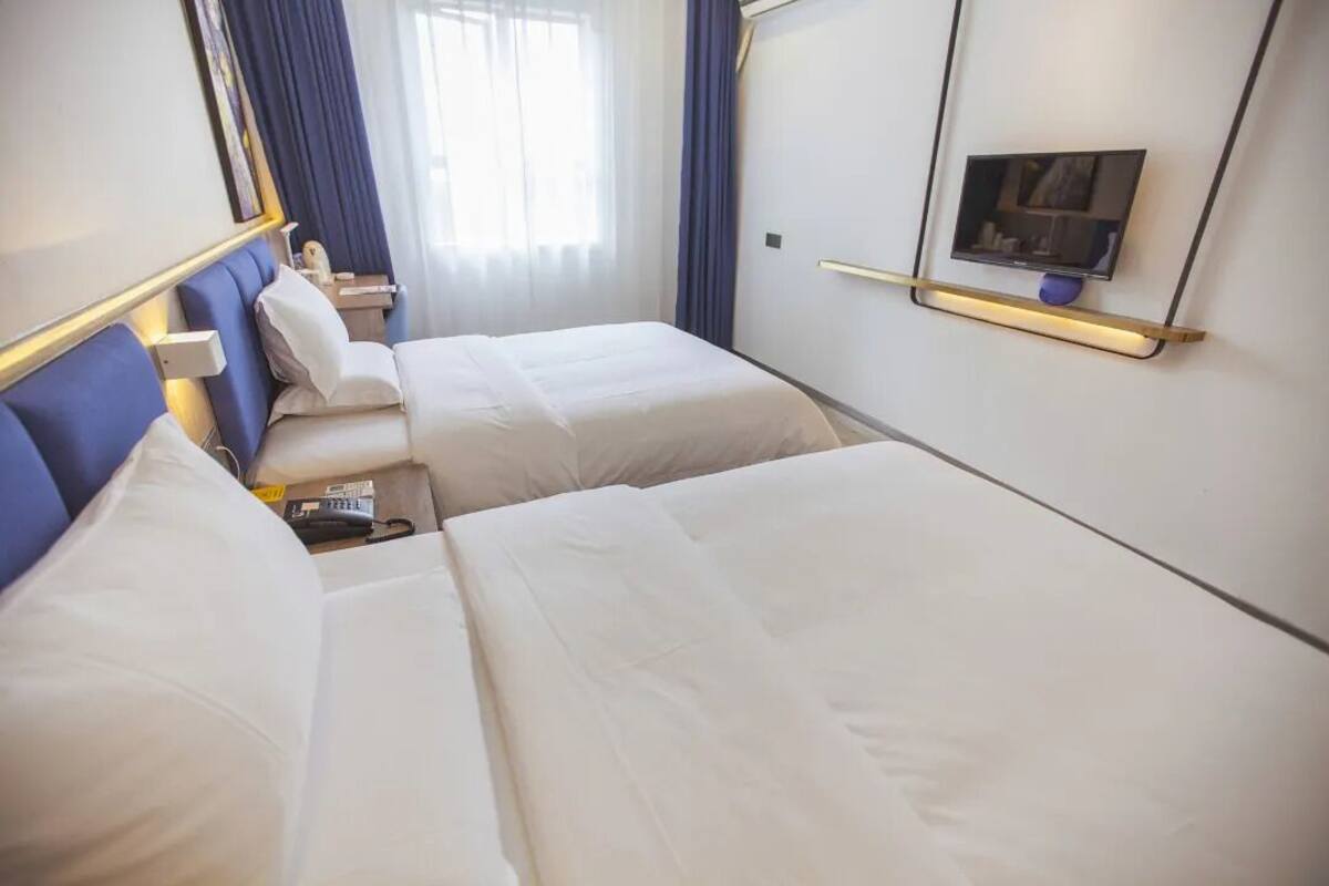 Quarto de hotel com duas camas, televisão presa na parede e janela com cortinas.