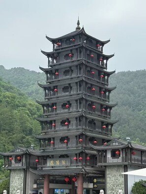A multi-tiered pagoda-style building with red lanterns, surrounded by lush greenery. - QīTiānYōupǐnZhāngjiājièDàyōngGǔchéngDiàn (Zhangjiajie)