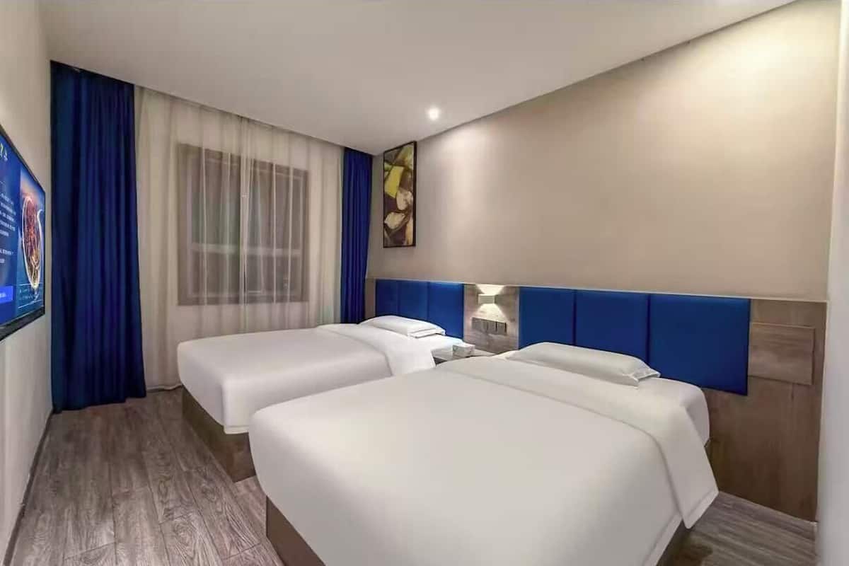 Quarto de hotel com duas camas, televisão, janela com cortinas e um quadro na parede.
