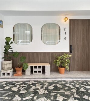Uma entrada moderna com duas janelas, um banco e plantas em vasos.