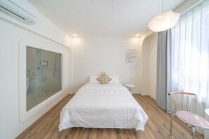 A hotel room with a large bed, a bedside table, a chair, a window with curtains, and an air conditioning unit. - Nantug (Tainan)