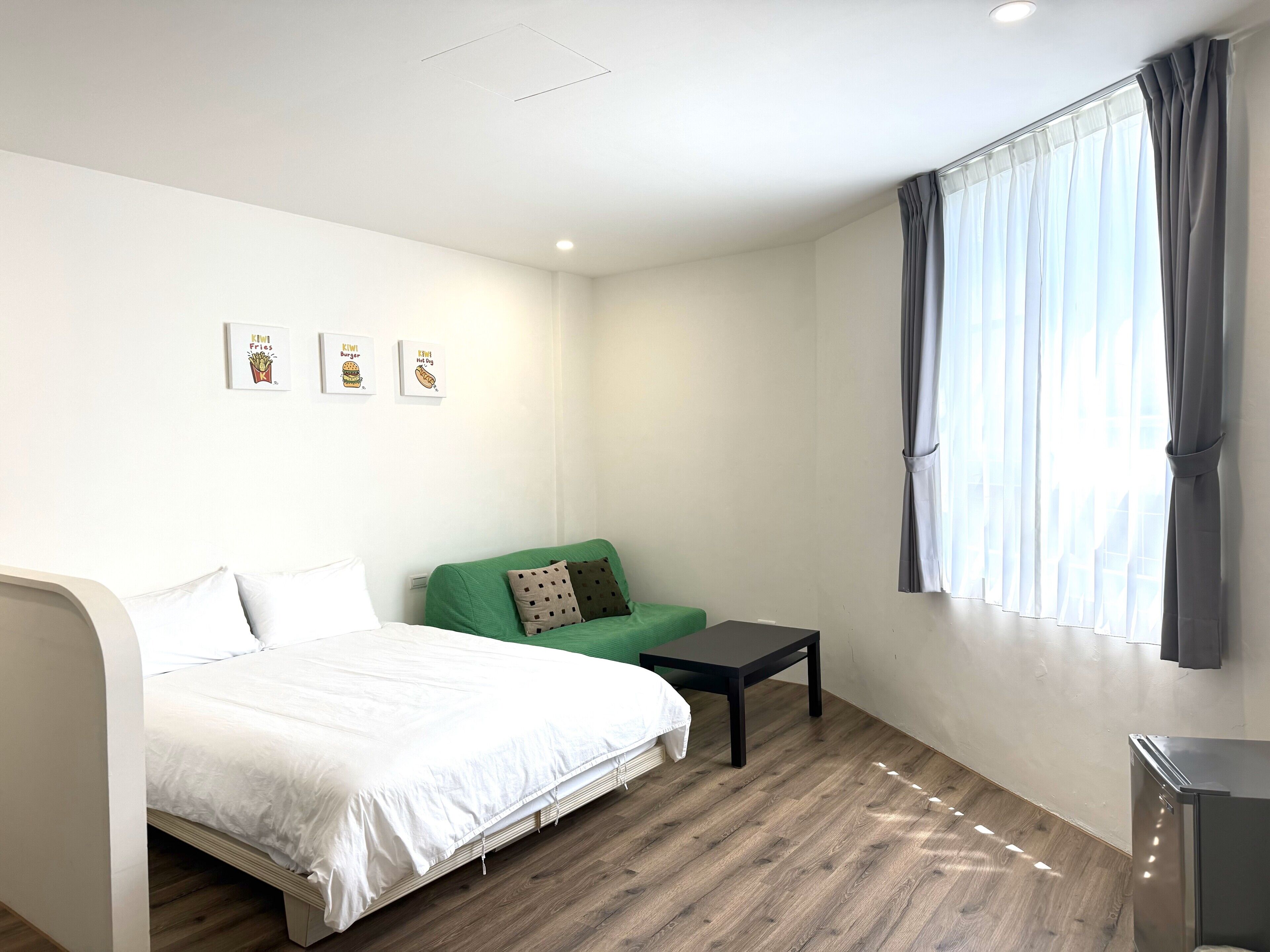 A bedroom with a bed, a green sofa, a small table, and a window with curtains.
