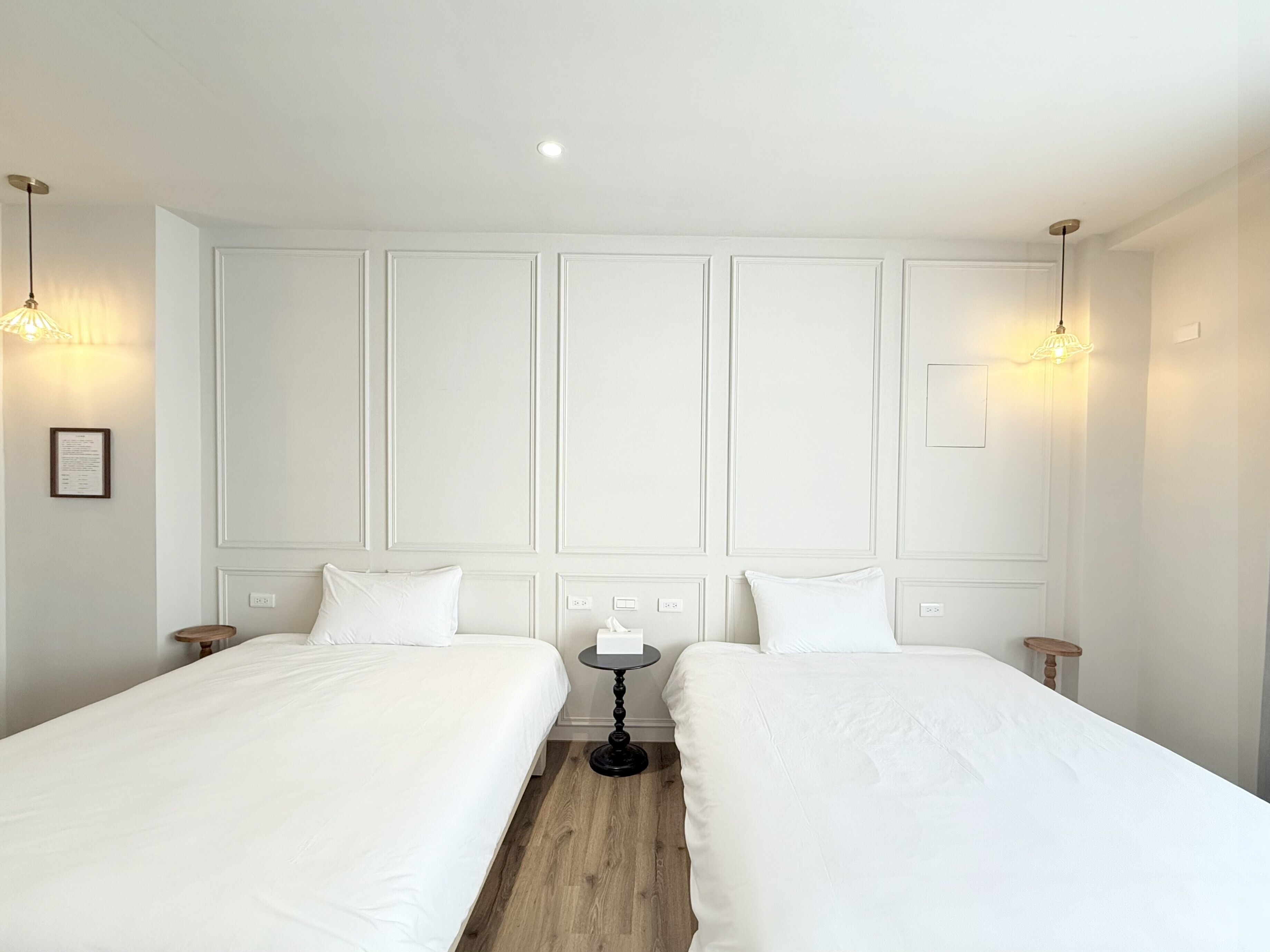 A hotel room with two single beds, a small round table, and pendant lighting.