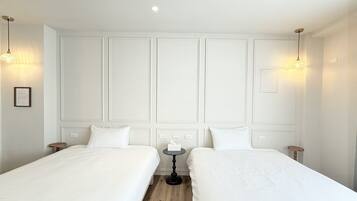 A hotel room with two single beds, a small round table, and pendant lighting.