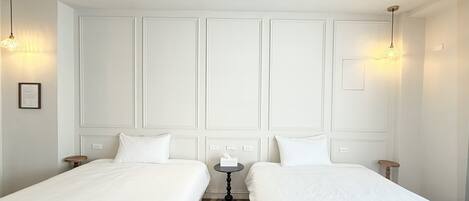 A hotel room with two single beds, a small round table, and pendant lighting.