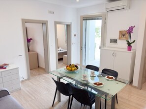 Un espace repas moderne avec une table en verre, des chaises noires, un panier de fruits et une orchidée en pot.