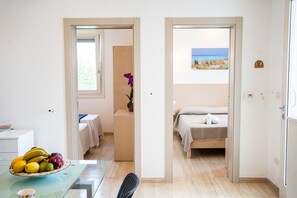 Une chambre avec un lit, un bureau sur lequel se trouve un panier de fruits, et une vue sur la plage par la fenêtre.