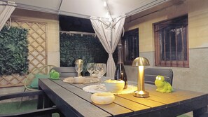 An outdoor dining area with a table set for two, featuring a bottle of wine, two wine glasses, a bowl of snacks, and a decorative lamp. - casa Anna by Ca-sa Check (Montichiari)
