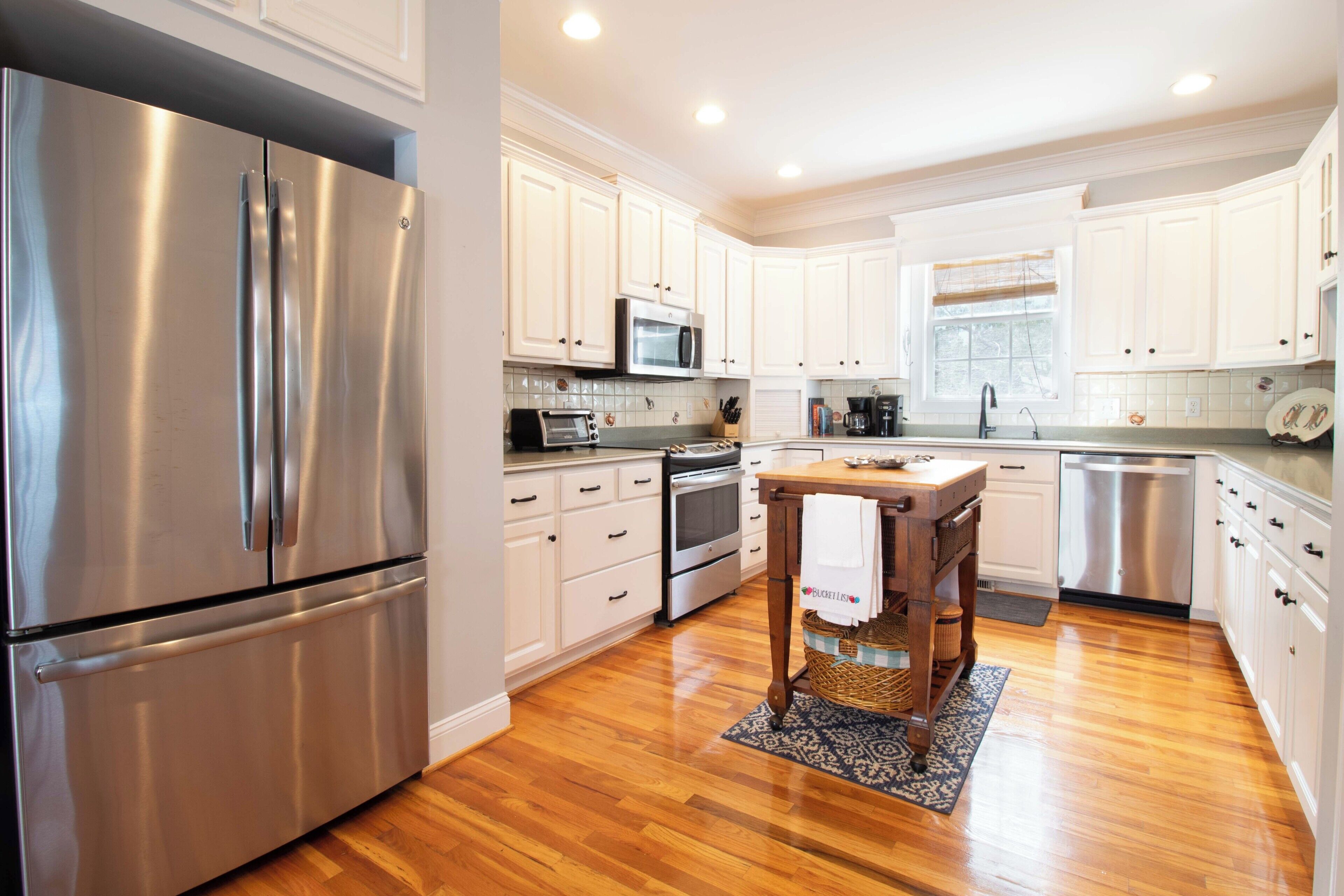 A modern kitchen with stainless steel appliances, white cabinetry, and a wooden dining table.