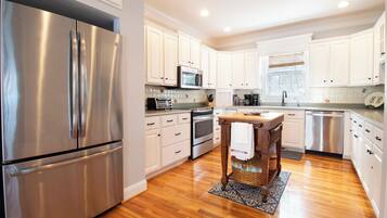 A modern kitchen with stainless steel appliances, white cabinetry, and a wooden dining table.