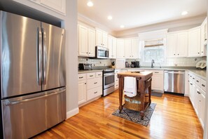 A modern kitchen with stainless steel appliances, white cabinetry, and a wooden dining table. - Bucket List - Beautiful golf course views (Edisto Island)