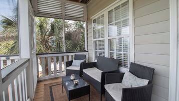 A covered porch with wicker furniture, a small table, and a view of palm trees.