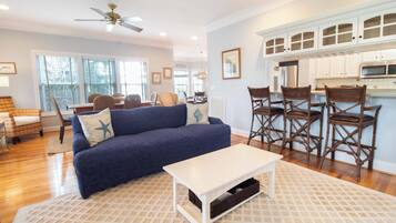 A living room with a blue sofa, a white coffee table, and a kitchen area with white cabinets and a microwave.