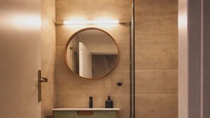 Ein modernes Badezimmer mit einem runden Spiegel, einem Waschbecken mit grüner Ablagefläche und einer bodentiefen Glasdusche.