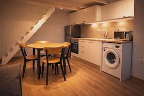 A compact kitchen with a washing machine, a microwave, and a dining area with chairs and a table.