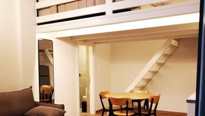 Ein Loft-Zimmer mit Etagenbett, Esstisch mit Stühlen, einer Couch und zwei kleinen Beistelltischen.