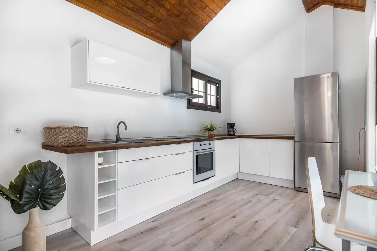 A modern kitchen with white cabinetry, a stainless steel refrigerator, and a wooden ceiling.