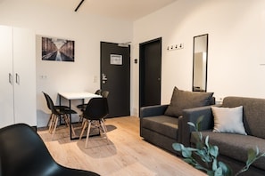 Ein modernes Wohnzimmer mit einer Couch, einem Esstisch mit Stühlen, einer schwarzen Tür und einem Spiegel an der Wand.