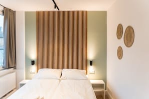 Een moderne hotelkamer met een bed, nachtkastjes, een houten lattenbalken hoofdeinde en decoratieve objecten aan de muur.