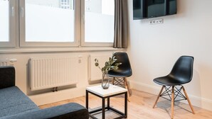 Ett modernt rum med en soffa, ett litet bord med en vas, en svart stol och en tv som är monterad på väggen.