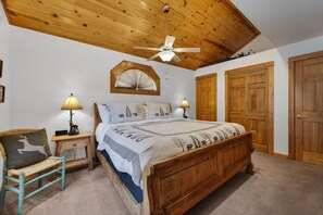 A bedroom with a wooden bed, two bedside lamps, a ceiling fan, and a large window. - Riverfront Condo • Fireplace • Close to RMNP (Estes Park)