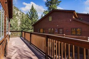 A wooden cabin with a deck and a mountain backdrop. - Riverfront Condo • Fireplace • Close to RMNP (Estes Park)