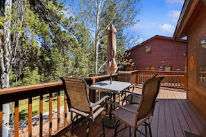 Une terrasse en bois avec des meubles d’extérieur, notamment une table et des chaises, ainsi qu’un grand parasol.
