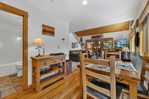 Un interior de madera con comedor, un banco de madera, una mesa con camino de mesa, una lámpara y un televisor.