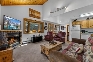 Un salón acogedor con chimenea, sillones de cuero, televisor y una zona de cocina.