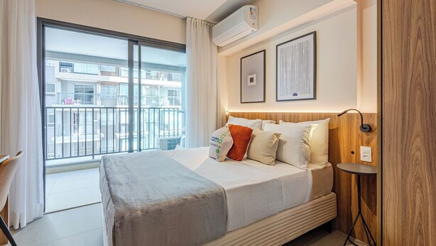 Ein Hotelzimmer mit großem Fenster, einem Bett mit Decke, einem Nachttisch und einer Wand-Klimaanlage.