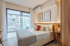 A hotel room with a large window, a bed with a blanket, a bedside table, and a wall-mounted air conditioner. - Roomo Transamerica SP Ibirapuera Sena Madureira (São Paulo)