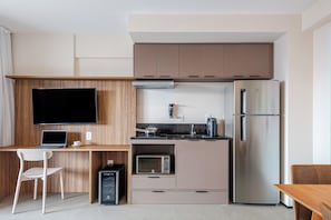 A modern kitchen with a flat-screen TV, a microwave, a refrigerator, and a wooden desk with a chair. - Roomo Transamerica SP Ibirapuera Sena Madureira (São Paulo)