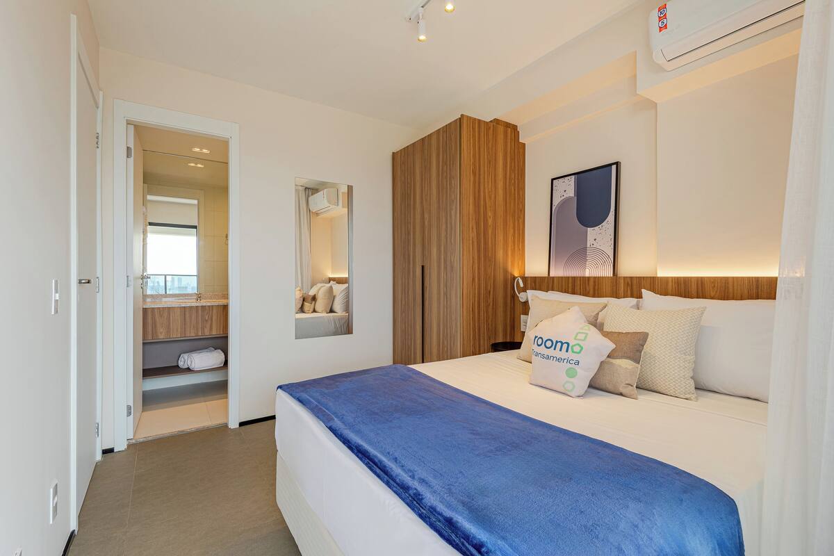 A hotel room with a bed, a wooden wardrobe, a mirror, and a wall-mounted artwork.