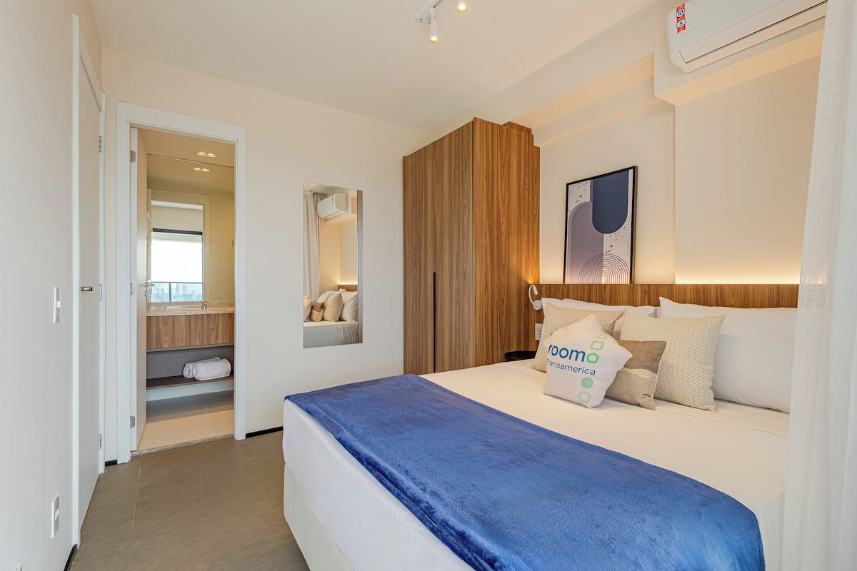 Habitación de hotel con cama, armario de madera, espejo y una obra de arte en la pared.
