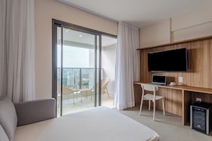 Una camera d'albergo con un letto, una scrivania con un portatile, una TV e vista sulla città attraverso una porta scorrevole.
