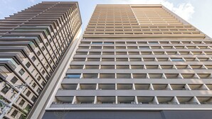 Ein Hochhaus mit modernem architektonischen Design, das mehrere Balkone und einen markanten Eingang aufweist.