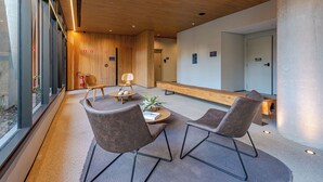 Eine moderne Lobby mit Holzboden, einer Sitzecke mit zwei Stühlen und einem Tisch sowie einer Bank entlang der Wand.